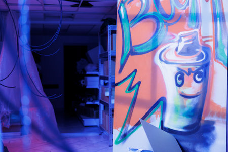 Rusty graffiti illuminated by bright neon lights in neglected old warehouse, empty chaotic place filled with spray paint art and fluorescent purple light. Damaged destroyed urban building.の写真素材