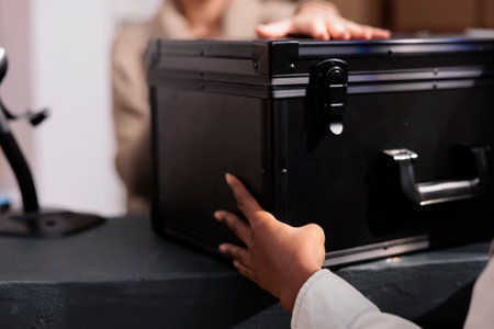 Retail store stockroom employee giving colleague black case at reception desk. Warehouse operator making customer order registration and checking product in stock at counter close upの写真素材