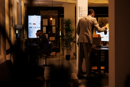 African american putting personal belongings in cardboard box after being fired from corporate job. Upset executive manager feeling depressed, leaving startup office late at night.の写真素材