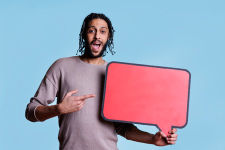 Excited arab man holding speech bubble to advertise product in red banner with copy space. Cheerful...