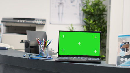 Laptop with blank green screen template at front desk, empty hospital reception counter for registration. Isolated chroma key display in medical facility lobby, blank mockup screen.の写真素材