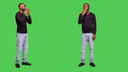 African american man sending air kisses on camera, posing with kissy face on full body greenscreen. Young adult being romantic in studio and doing flirty gesture, optimistic reaction.の写真素材