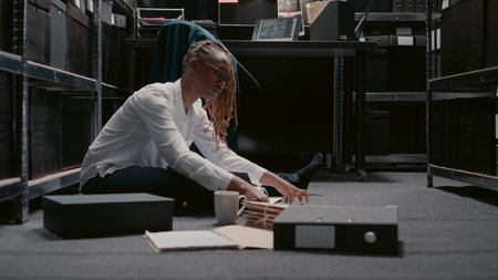 African american detective examining case files in archive room, working on private investigation. Young inspector using suspicious forensic evidence and surveillance footage to do research.の写真素材