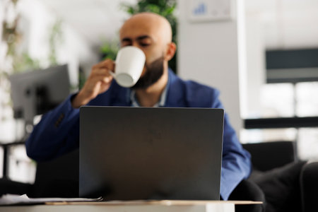 Arab employee drinking coffee and working at start up product development on laptop. Young man...