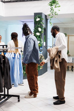 Clothing store employee examining shirt on customer and checking fit. African american man choosing...