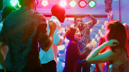 Diverse group of friends at nightclub, dancing on electronic mix from DJ music station in discotheque. Funky people partying and enjoying modern audio sounds, colorful discolights.の写真素材