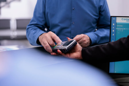 Senior patient typing credit card pin on pos paying for medication treatment and examination during checkup visit in hospital waiting room. Health care service support and conceptの写真素材