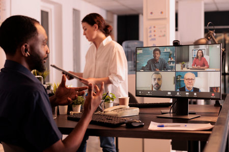 African american man speaking to remote team on videocall, attending online meeting, company strategy discussion on videconference on computer. Coworkers talking on teleconference at nightの写真素材
