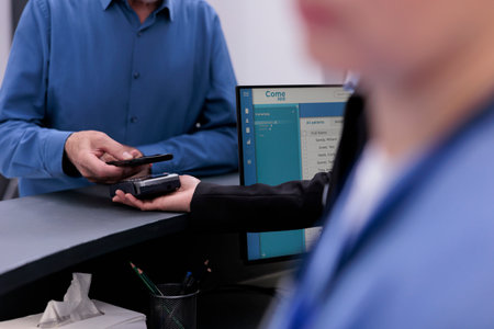 Close up of elderly patient putting mobile phone on pos paying for health care treatment and...