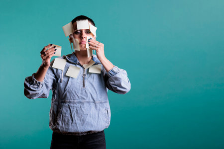 Portrait of stressed overworked woman with sticky notes all over her body, having the duty to remember work details. Frustrated depressed female posing in studio standing over isolated backgroundの写真素材