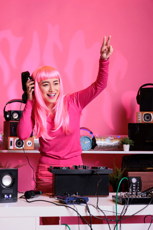 Artist with pink hair performing eletronic music in club during night time having fun while mixing song at professional mixer console. Woman standing at dj table doing performance with audio equipmentの写真素材