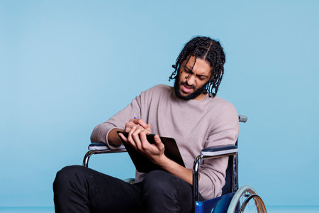 Confused arab man in wheelchair holding pen and clipboardの写真素材