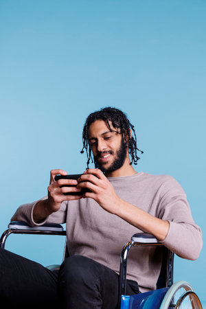 Cheerful arab gamer in wheelchair playing on mobile phone