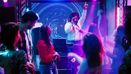 Happy people attending disco party, dancing and having fun on dace floor at club. Young men and women jumping on electronic music at celebration event, discolights. Handheld shot.の写真素材