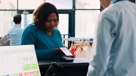 African american client paying for casual wear with mobile phone nfc on pos terminal, buying...
