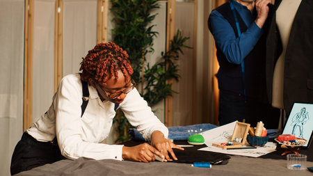 Apprentice measuring fabric in atelier, learning to create clothes from experienced luxury couturier. Old craftsman teaching tailoring skills to student, beginner working in tailor workshop.の写真素材