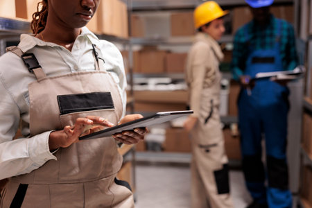 Storehouse supervisor doing inventory operations in digital tablet app. African american storehouse employee hands clicking on portable device screen, using stock managing applicationの写真素材