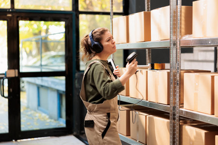 Small business employee scanning carton boxes barcode using store scanner, listening music during warehouse inventory. Worker looking at storehouse shelves, preparing clients orders for deliveryの写真素材