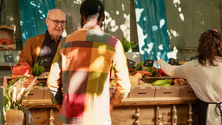 Happy female seller hugging and greeting loyal customer, feeling positive at food marketplace. Young women sharing hug at farmers market, enjoying visit from regular client. Handheld shot.の写真素材