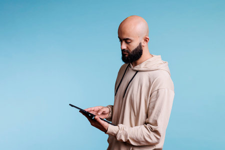 Young concentrated arab man working on digital tablet, typing online message. Focused person reading online on portable electronic gadget, scrolling internet pages and textingの写真素材