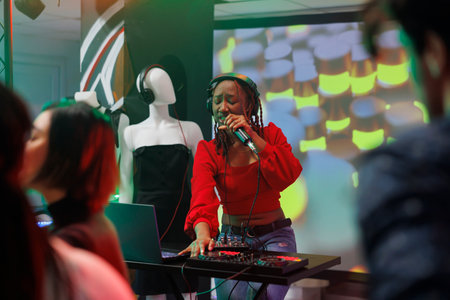 Woman singer mixing techno sounds with dj station on stage while performing at nightclub party. African american musician wearing headphones singing in microphone in clubの写真素材