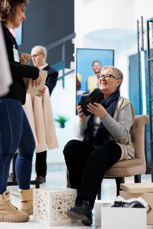 Senior woman trying fashionable black shoes, shopping for formal wear in clothing store. Elderly customer buying stylish clothes and merchandise in modern boutique. Commercial activity conceptの写真素材