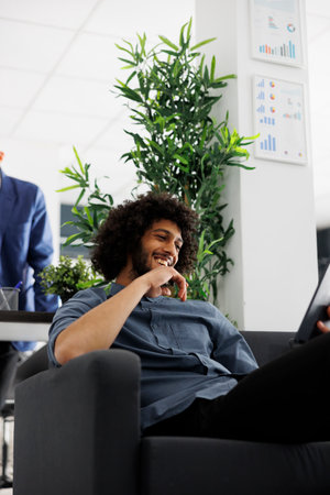 Arab start up entrepreneur laughing while talking in online meeting on digital tablet in office. Smiling business company worker using corporate videocall application to chat with coworkersの写真素材