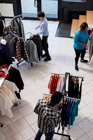 Top view of people shopping for clothes in modern boutique, looking at hangers full with stylish merchandise, Diverse customers checking new fashion collection, analyzing items fabricの写真素材