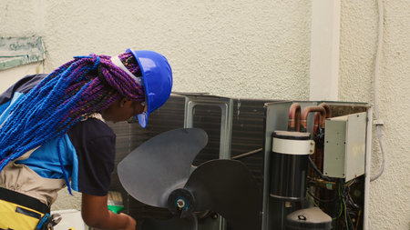 Seasoned mechanic commissioned for outdoor hvac system routine cleaning and maintenance, using soft dusting brush to sweep away built up layer of dirt and debris from blower fanの写真素材