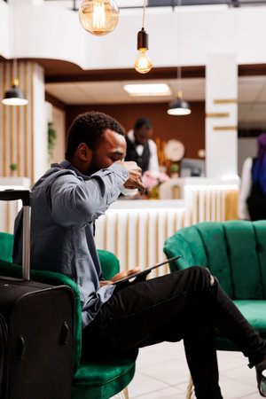 African American businessman drinking coffee and resting while waiting for check-in hotel lobby, black guy tourist holding digital tablet checking in online. Travel, vacation and business tripの写真素材