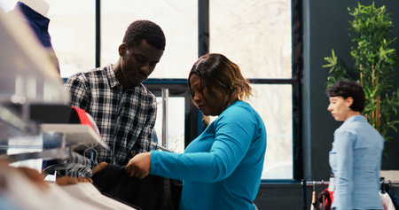 Stylish couple looking at trendy clothes, checking shirt fabric in modern boutique. African american...