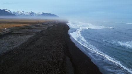 Icelandic black sand beach drone shot, beautiful coastline with waves crashing on atlantic shore. Nordic landscape with snowy mountains and black sand on beaches, scenic route. Slow motion.の写真素材