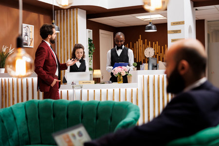 Guest asking hotel staff about services, ensuring pleasant stay and comfortable accommodation. Man travelling for work, employees providing great local recommendations after check in process.の写真素材