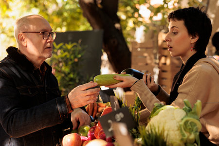 Woman vendor selling organic bio fruits and vegetables at local farmers market stand, small business. Food market seller showing fresh veggies to senior customer, farming store.の写真素材