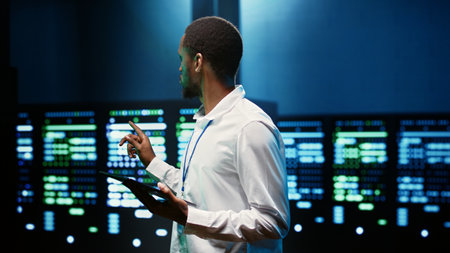 African american supervisor in server farm using tablet to find firewall misconfigurations affecting...