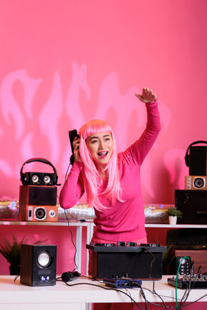 Asian artist with pink hair dancing and having fun in club while playing techno music at professional mixer console, enjoying night lifestyle. Performer doing performance with audio equipmentの写真素材