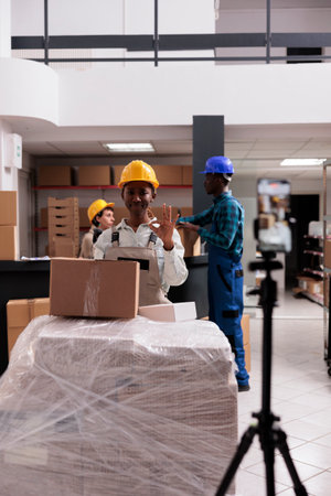 Storehouse employee shooting stock checking video and showing ok gesture with fingers. Retail storehouse workers doing goods inventory and looking at mobile phone camera with okay signの写真素材
