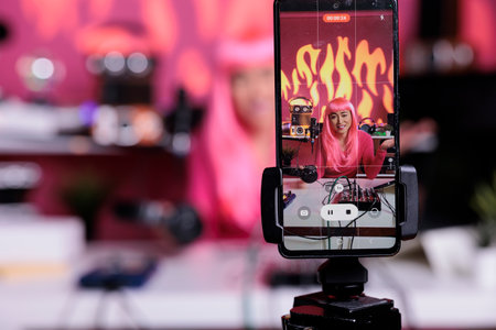 Influencer recording podcast using professional vlogging equipment while standing in streaming studio, posting vlog on social media to gain subscribers. Asian creator filming vlog with phone cameraの写真素材
