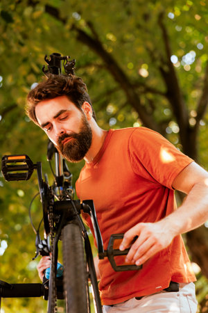 Detailed shot showcasing athletic caucasian man accurately adjusting and securing bicycle pedal and crank arm. Close-up view of male cyclist doing yearly maintenance on bike components in yard.の写真素材