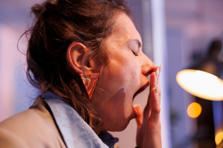 Tired businesswoman working overhours at company strategy in startup office, analyzing financial graphs on computer. Overworked entrepreneur developing investment plan to increase profitの写真素材