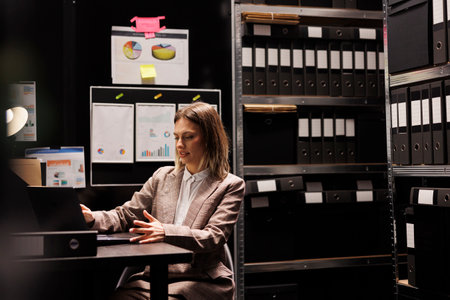 Corporate manager working at administrative record, analyzing business paperwork in arhive room. Caucasian businesswoman checking bureaucracy report, searching accountancy files. Depository conceptの写真素材