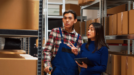 Young adult with crutches analyzing boxes with owner, using tablet to do merchandise logistics in storage room. Asian man talking to entrepreneur about products, physical disability.の写真素材