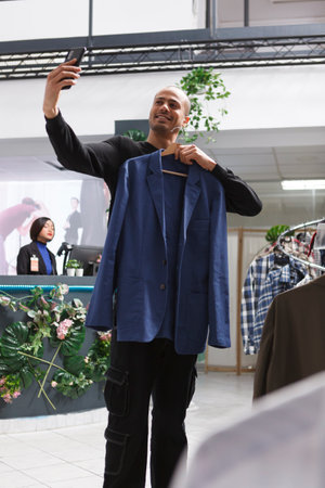 Clothing store arab man client holding jacket on hanger and taking photo on smartphone while...
