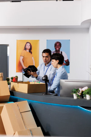 Store workers putting trendy clothes in cardboard boxes, preparing packages for delivery in modern...