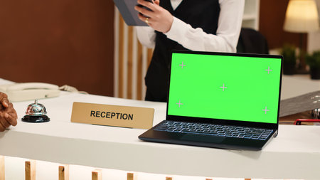 Close up of african american guest ringing service bell next to laptop chroma key green screen mock up at reception during check in process. Tourist ready to book in reservation at hotel front deskの写真素材