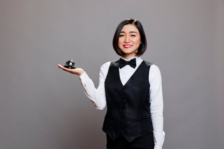 Restaurant receptionist in uniform holding bell in hand, smiling and looking at camera. Catering...