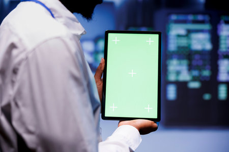 Engineer investigating performance trends in data center. Professional using green screen tablet to identify operational challenges in server hub contributing to hardware malfunction, close upの素材