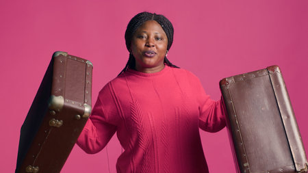 Female african american traveler with confidence proudly displays fashionable brown suitcases. Stunning black woman with vibrant smile grasps two pieces of luggage ready to travel in style.の写真素材