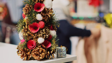 Extreme close up shot of festive miniature Christmas tree adorned with pine cones and flowers sitting on clothing store counter during winter holiday season. Xmas decor in fashion boutiqueの写真素材