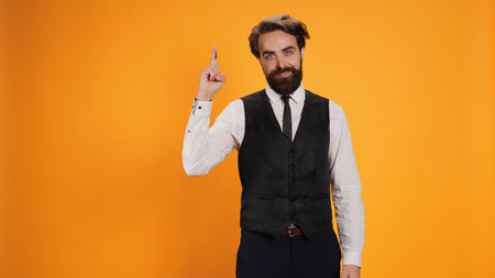 Elegant butler points up on camera, showing something above head while he wears formal attire for...